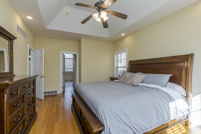 bedroom with a tray ceiling, ceiling fan, and light wood-type flooring