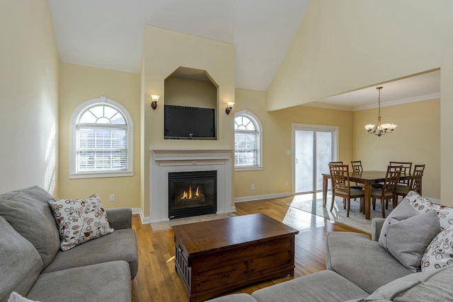 living room with light wood-type flooring, an inviting chandelier, a wealth of natural light, and ornamental molding