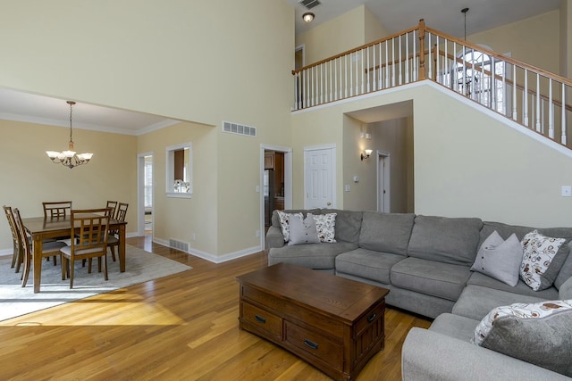 living room featuring an inviting chandelier, a towering ceiling, ornamental molding, and light wood-type flooring