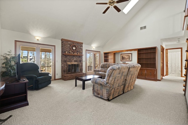 carpeted living room with a brick fireplace, a skylight, high vaulted ceiling, and ceiling fan