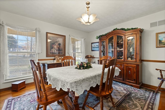 dining area with plenty of natural light, wood-type flooring, and an inviting chandelier