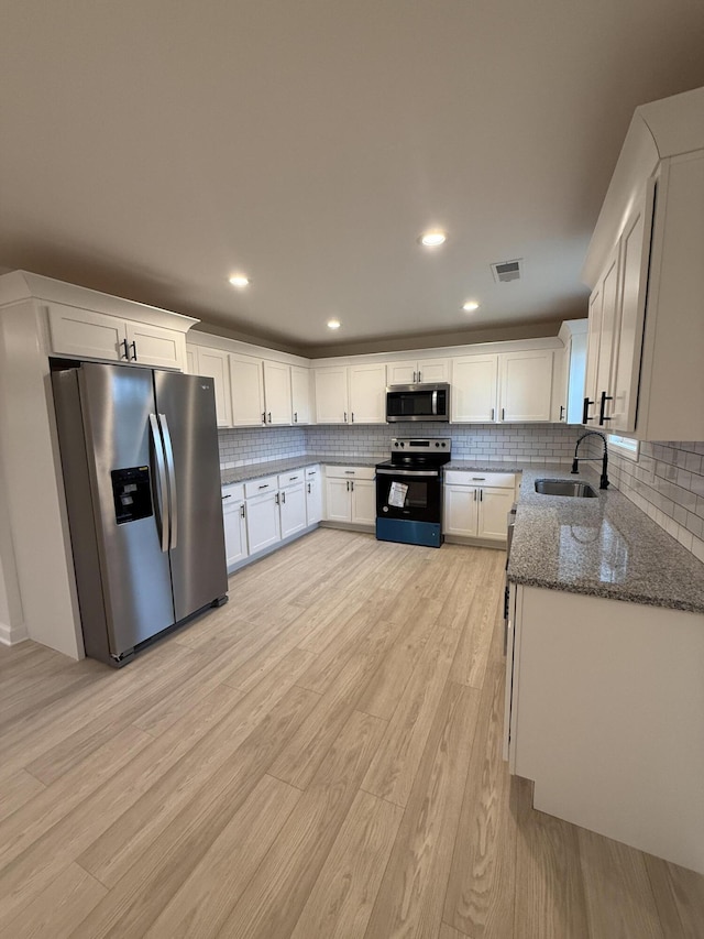 kitchen featuring stainless steel appliances, sink, stone countertops, light hardwood / wood-style flooring, and white cabinetry