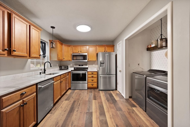 kitchen featuring sink, hanging light fixtures, washing machine and dryer, appliances with stainless steel finishes, and dark hardwood / wood-style flooring