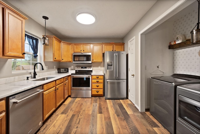 kitchen with sink, stainless steel appliances, pendant lighting, washer and clothes dryer, and hardwood / wood-style flooring