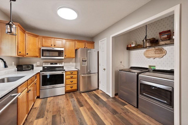 kitchen with appliances with stainless steel finishes, dark wood-type flooring, sink, washer and dryer, and decorative light fixtures