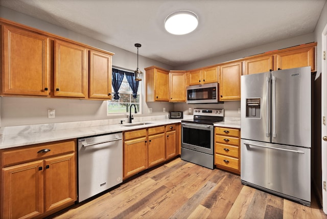 kitchen with sink, stainless steel appliances, decorative light fixtures, and light hardwood / wood-style floors