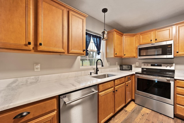 kitchen with light wood-type flooring, stainless steel appliances, hanging light fixtures, and sink