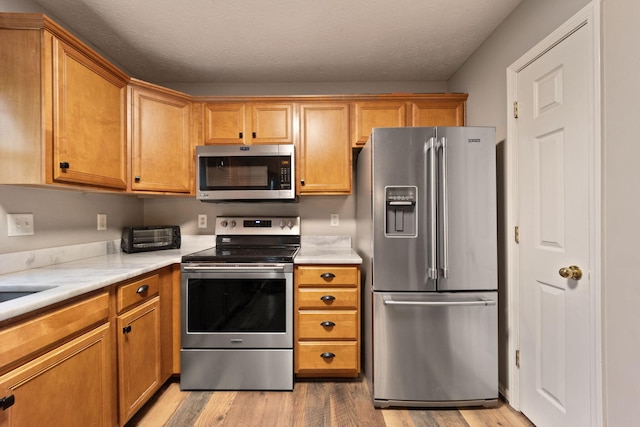 kitchen with a textured ceiling, light hardwood / wood-style floors, and stainless steel appliances