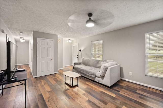 living room featuring ceiling fan, a healthy amount of sunlight, dark hardwood / wood-style flooring, and a textured ceiling