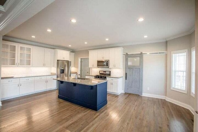 kitchen featuring white cabinetry, a barn door, light hardwood / wood-style flooring, a kitchen island with sink, and appliances with stainless steel finishes