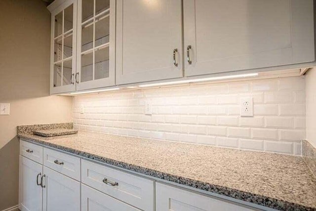 kitchen featuring decorative backsplash, light stone countertops, and white cabinetry