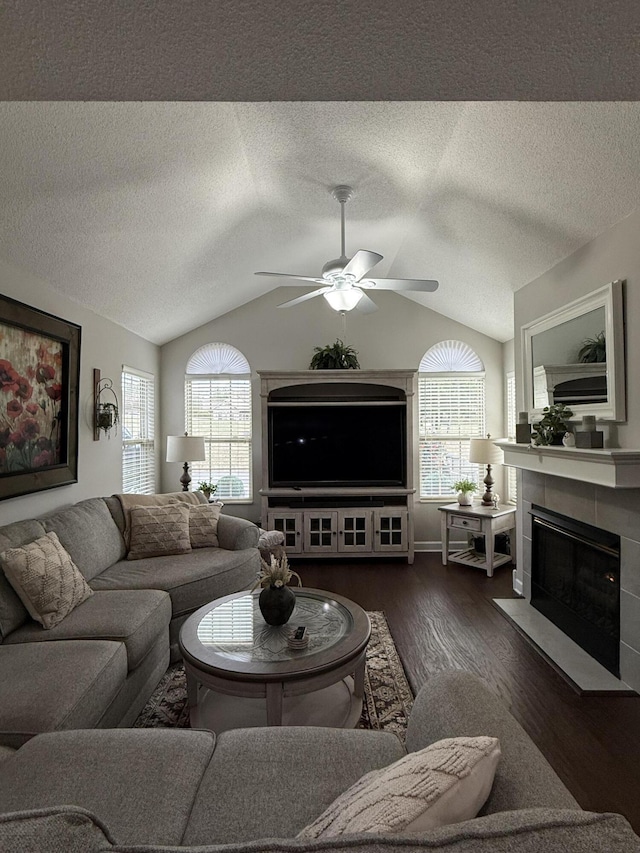 living room featuring vaulted ceiling, dark hardwood / wood-style floors, ceiling fan, a textured ceiling, and a tiled fireplace