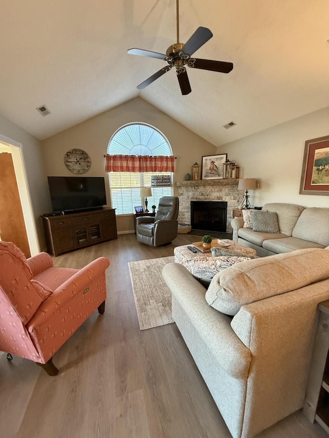 living room with ceiling fan, lofted ceiling, dark hardwood / wood-style floors, and a stone fireplace