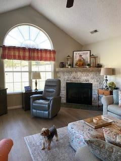 living room with hardwood / wood-style flooring, vaulted ceiling, ceiling fan, and a fireplace