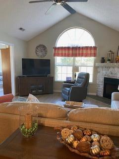 living room featuring lofted ceiling, a fireplace, and ceiling fan