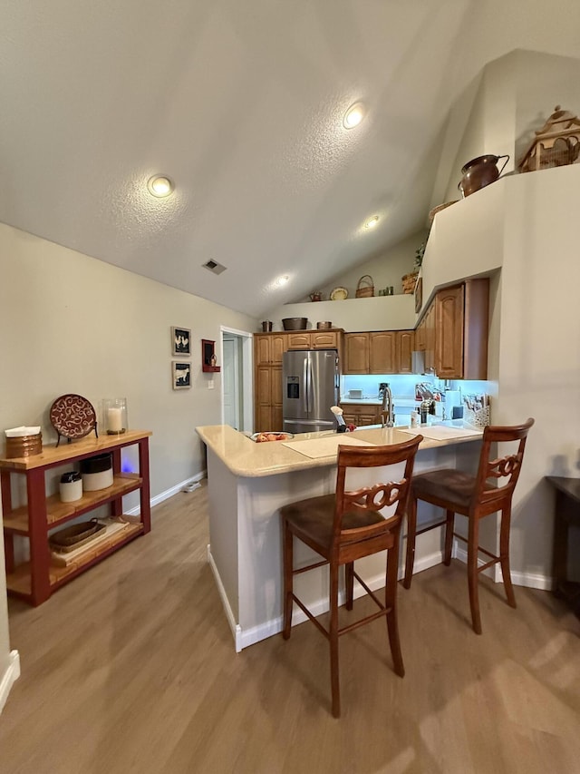 kitchen with stainless steel fridge, a kitchen bar, kitchen peninsula, a textured ceiling, and light wood-type flooring