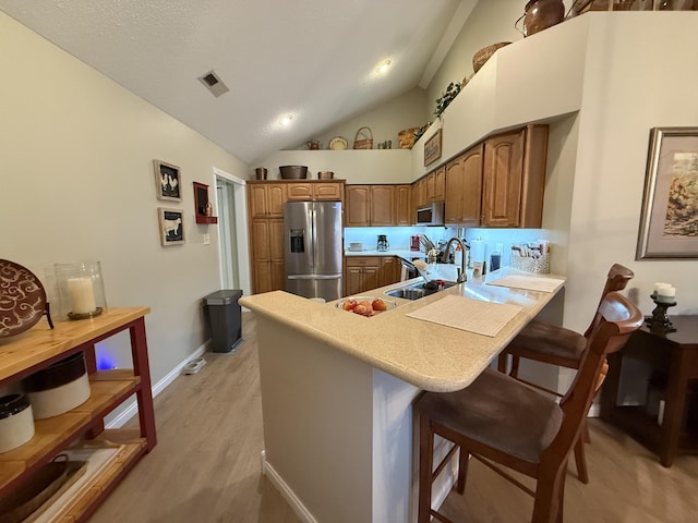 kitchen featuring sink, a breakfast bar area, stainless steel appliances, light hardwood / wood-style floors, and kitchen peninsula