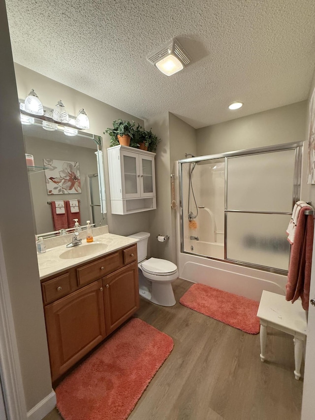 full bathroom featuring bath / shower combo with glass door, hardwood / wood-style floors, vanity, and a textured ceiling