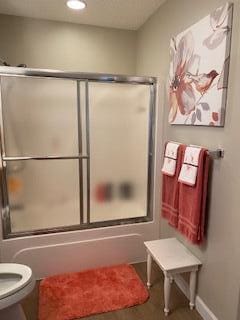 bathroom featuring shower / bath combination with glass door and toilet