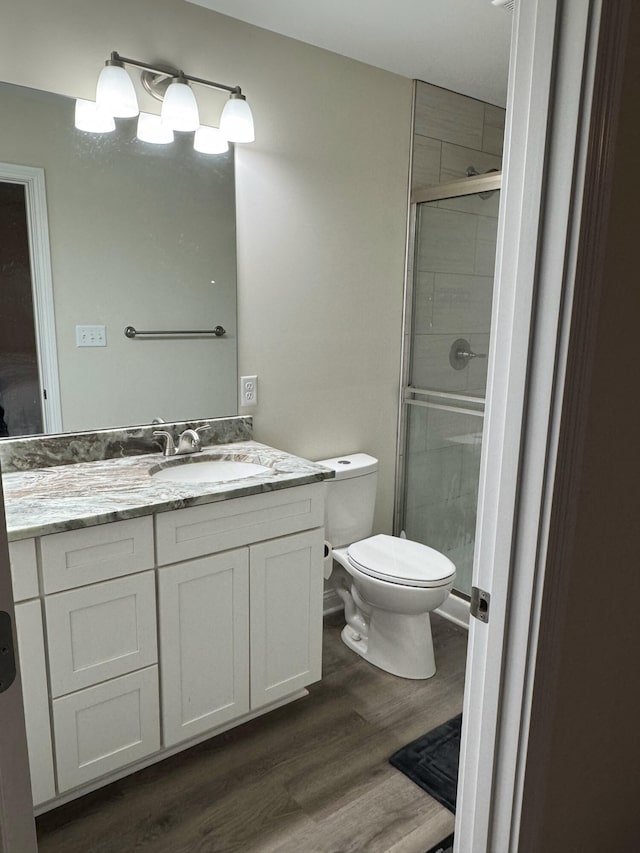 bathroom with hardwood / wood-style floors, vanity, a shower with door, and toilet