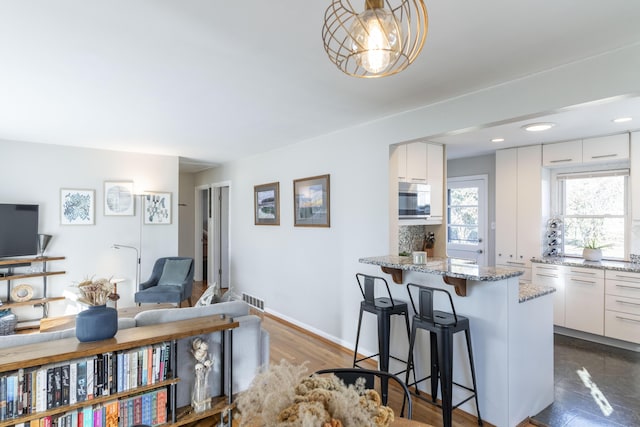 kitchen with hanging light fixtures, light stone countertops, dark hardwood / wood-style flooring, white cabinetry, and a breakfast bar area