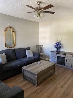 living room with ceiling fan, dark wood-type flooring, and a textured ceiling