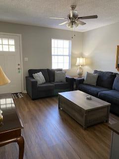 living room with a textured ceiling, ceiling fan, and dark wood-type flooring