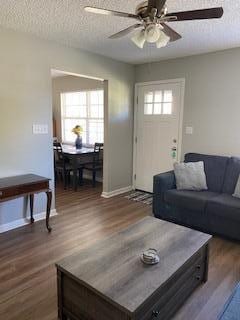 living room with a textured ceiling, dark hardwood / wood-style flooring, a wealth of natural light, and ceiling fan