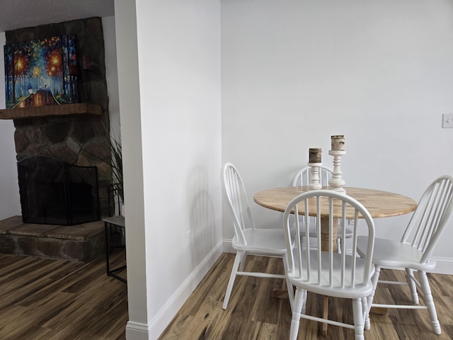 dining area with hardwood / wood-style floors and a stone fireplace