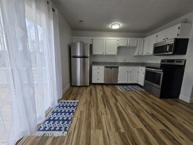 kitchen with appliances with stainless steel finishes, dark hardwood / wood-style flooring, white cabinetry, and sink