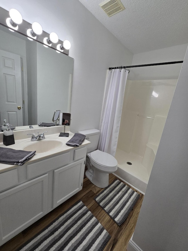 bathroom featuring walk in shower, vanity, a textured ceiling, hardwood / wood-style floors, and toilet