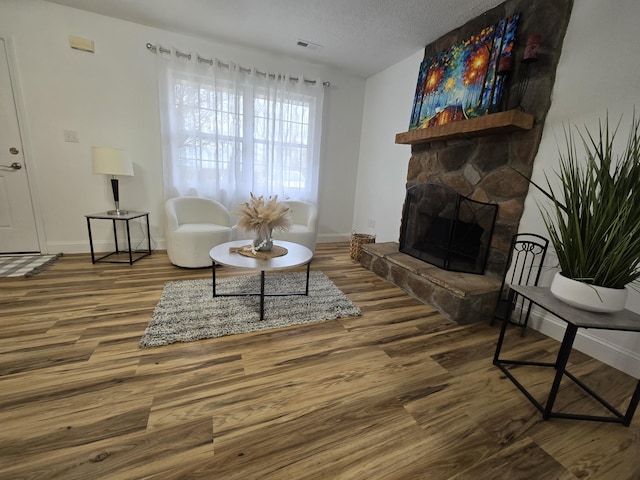 living room featuring hardwood / wood-style floors, a textured ceiling, and a stone fireplace