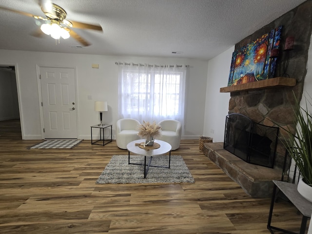 living room with dark hardwood / wood-style floors, ceiling fan, a stone fireplace, and a textured ceiling