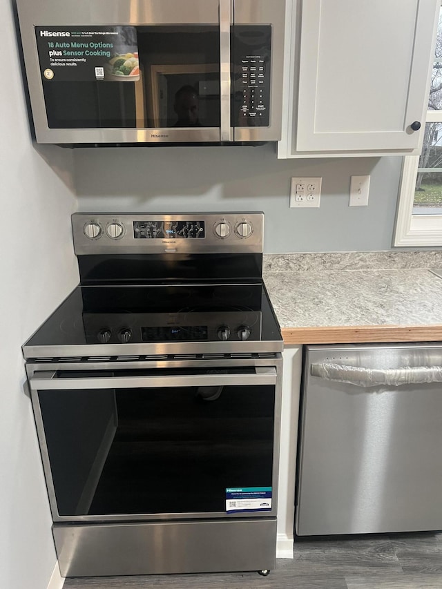 kitchen with appliances with stainless steel finishes, white cabinetry, and hardwood / wood-style floors