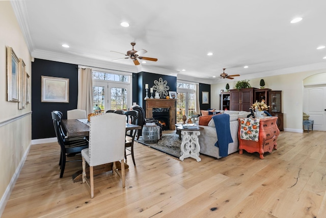 dining area with a lit fireplace, light wood finished floors, and ornamental molding