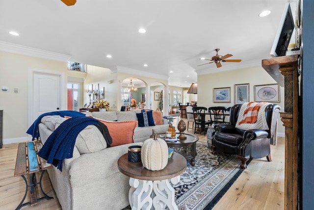 living area with light wood-type flooring, arched walkways, ornamental molding, and ceiling fan with notable chandelier