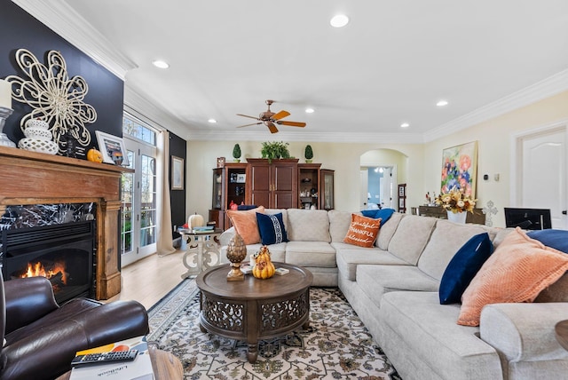 living room featuring a high end fireplace, crown molding, recessed lighting, light wood-style floors, and arched walkways