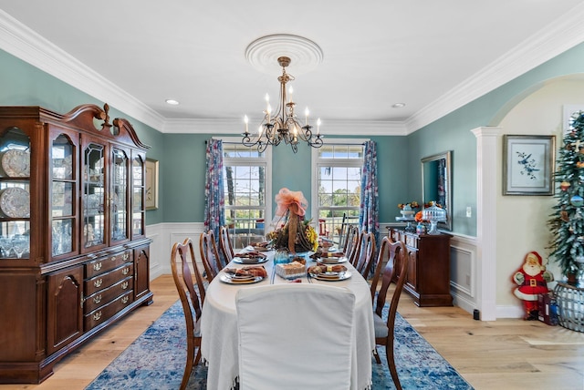 dining area with light wood finished floors, a chandelier, wainscoting, and crown molding