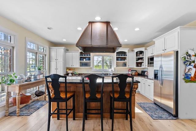 kitchen with dark countertops, appliances with stainless steel finishes, island range hood, white cabinetry, and open shelves