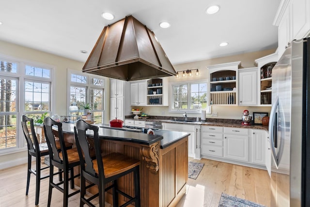 kitchen featuring open shelves, light wood-type flooring, freestanding refrigerator, exhaust hood, and a sink