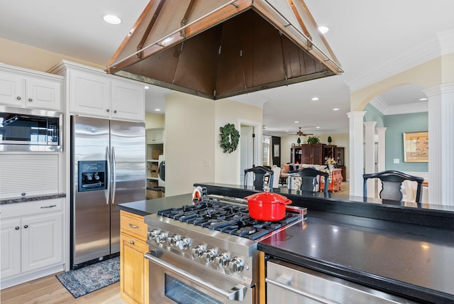 kitchen with under cabinet range hood, dark countertops, white cabinetry, appliances with stainless steel finishes, and decorative columns