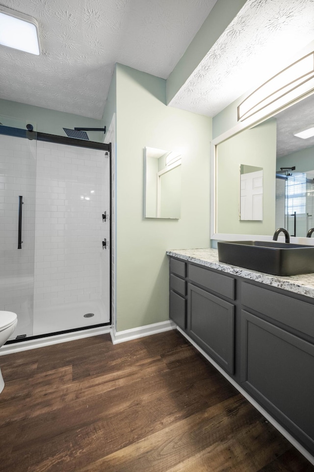 bathroom with vanity, hardwood / wood-style flooring, toilet, a textured ceiling, and walk in shower