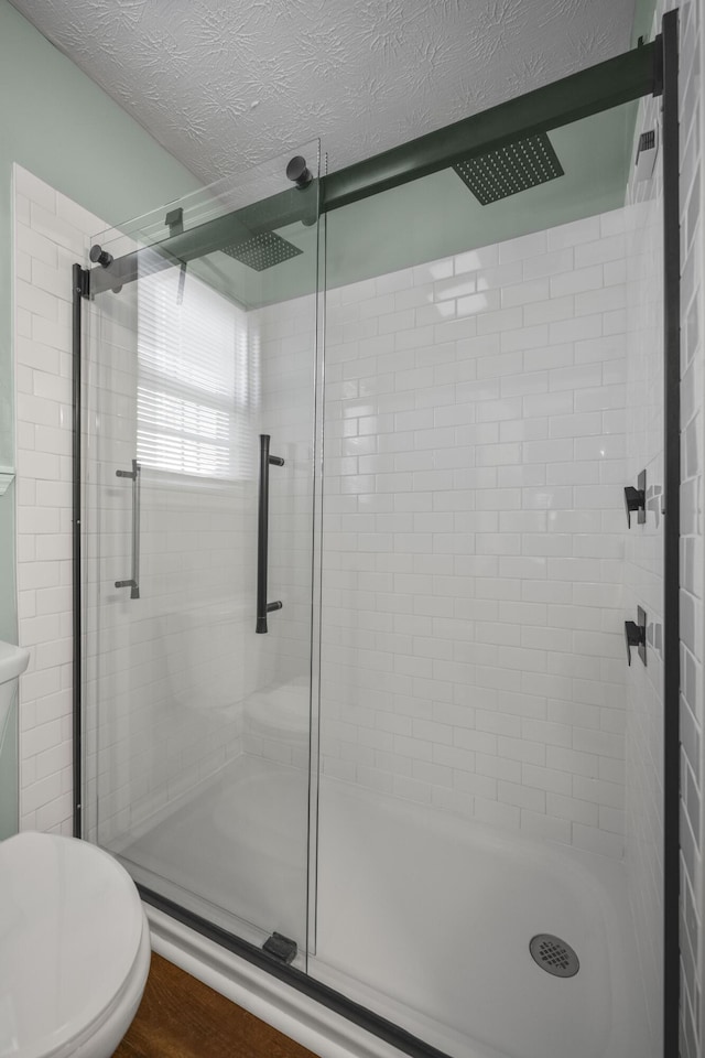 bathroom with hardwood / wood-style floors, a shower with shower door, a textured ceiling, and toilet