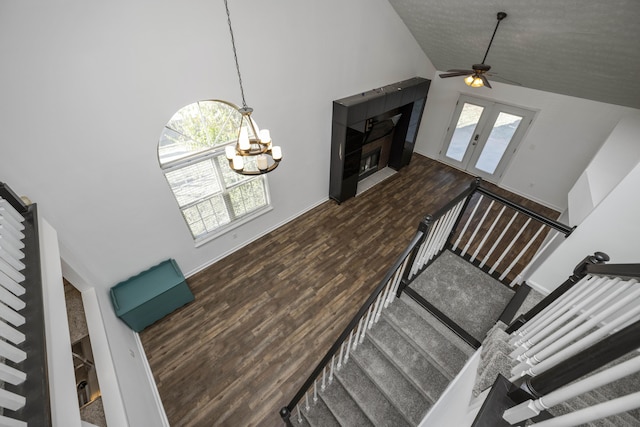 staircase featuring french doors, hardwood / wood-style floors, high vaulted ceiling, and ceiling fan with notable chandelier