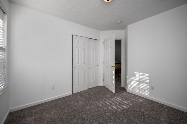 unfurnished bedroom featuring dark colored carpet, a textured ceiling, and a closet