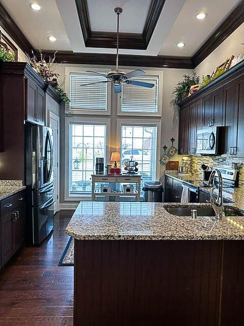 kitchen featuring dark wood-type flooring, crown molding, appliances with stainless steel finishes, light stone counters, and dark brown cabinetry