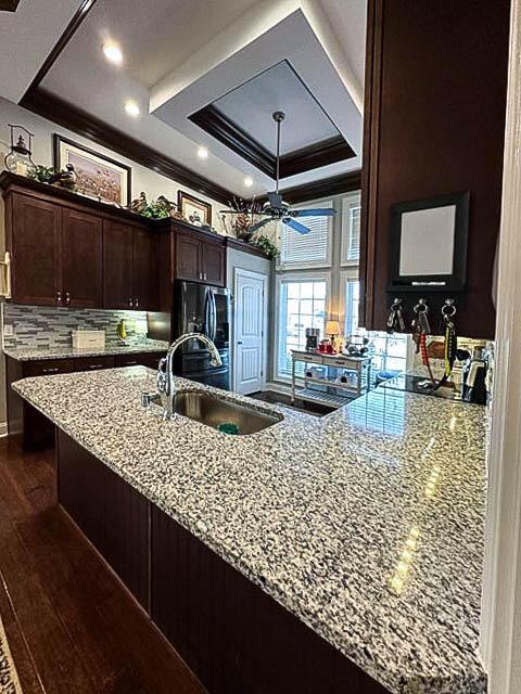 kitchen featuring light stone counters, a raised ceiling, sink, dark hardwood / wood-style floors, and stainless steel refrigerator