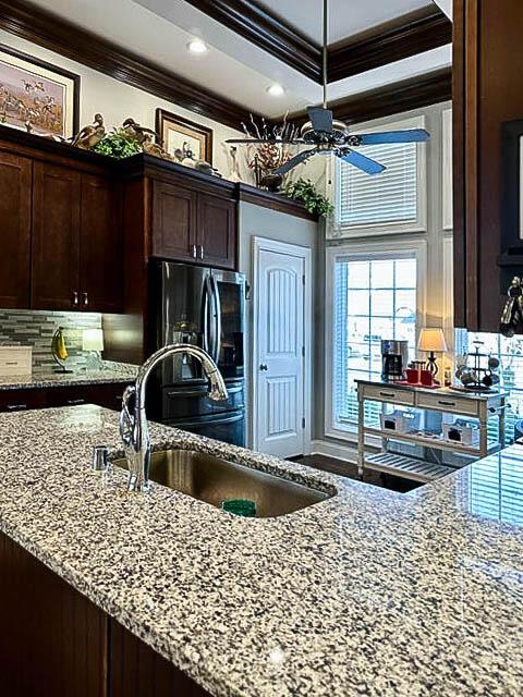 kitchen featuring stainless steel fridge with ice dispenser, light stone countertops, ornamental molding, and sink