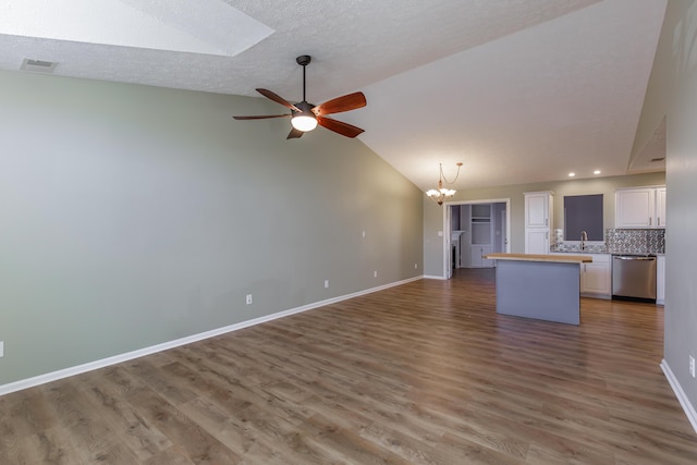 unfurnished living room featuring hardwood / wood-style floors, ceiling fan with notable chandelier, lofted ceiling with skylight, and sink