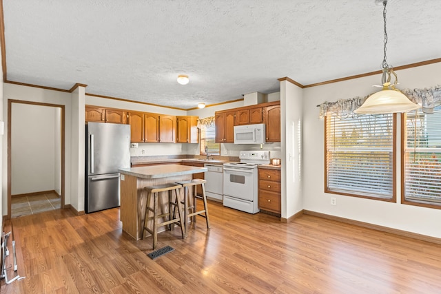 kitchen with crown molding, white appliances, light hardwood / wood-style floors, a kitchen island, and decorative light fixtures